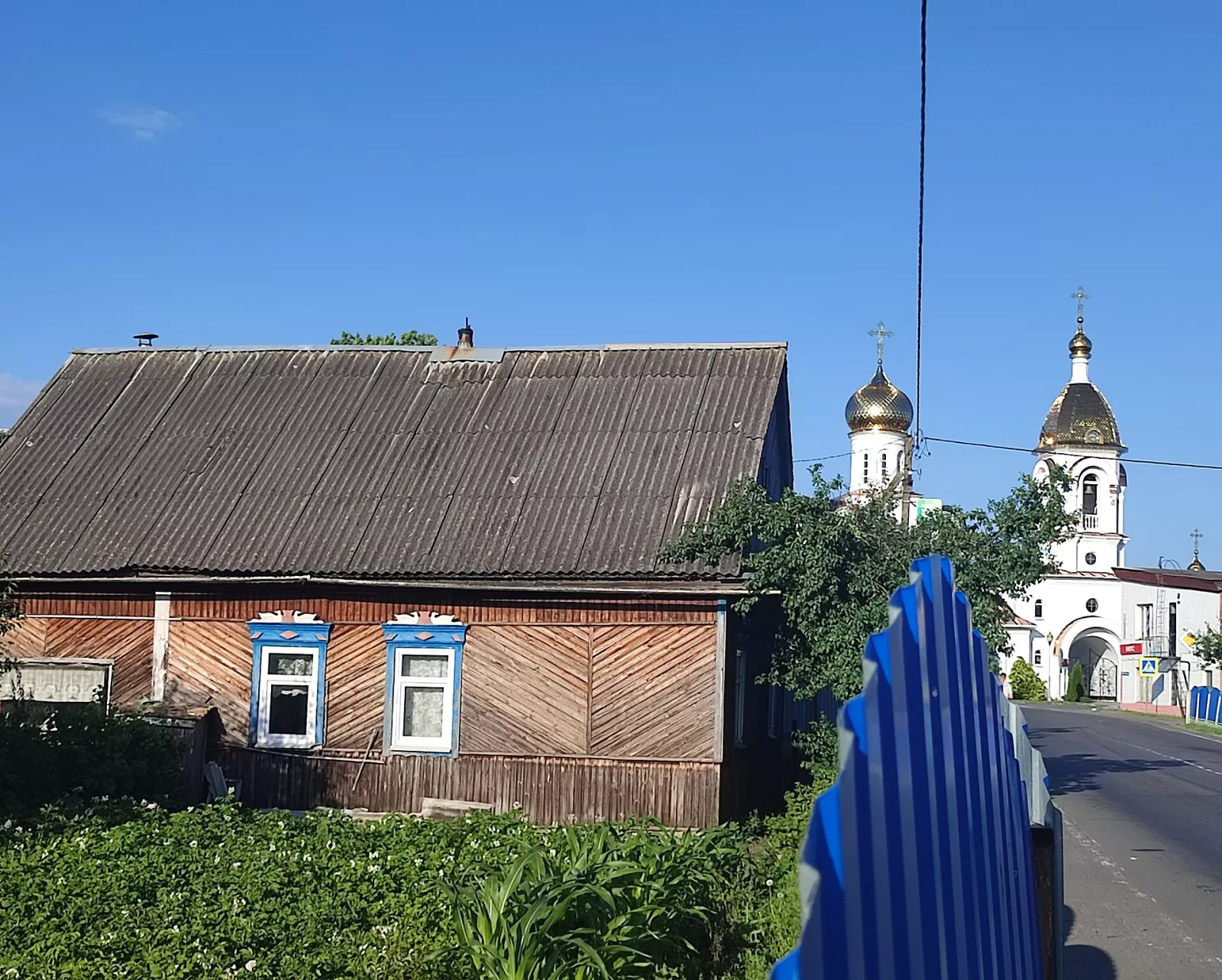 Дерев’яна хата з різьбленими лиштвами на вулиці Турова, позаду білий храм