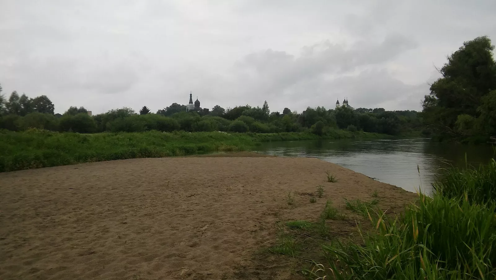 Піщаний берег Бугу, за річкою бані церкви й вежі костелу Влодави