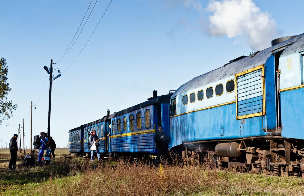 Синій вузькоколійний потяг з тепловозом на станції Зарічне, біля нього пасажири