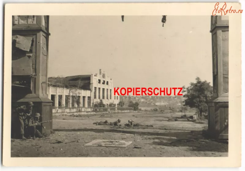 Німецькі солдати біля арки, позаду пошкоджений корпус фабрики, 1941